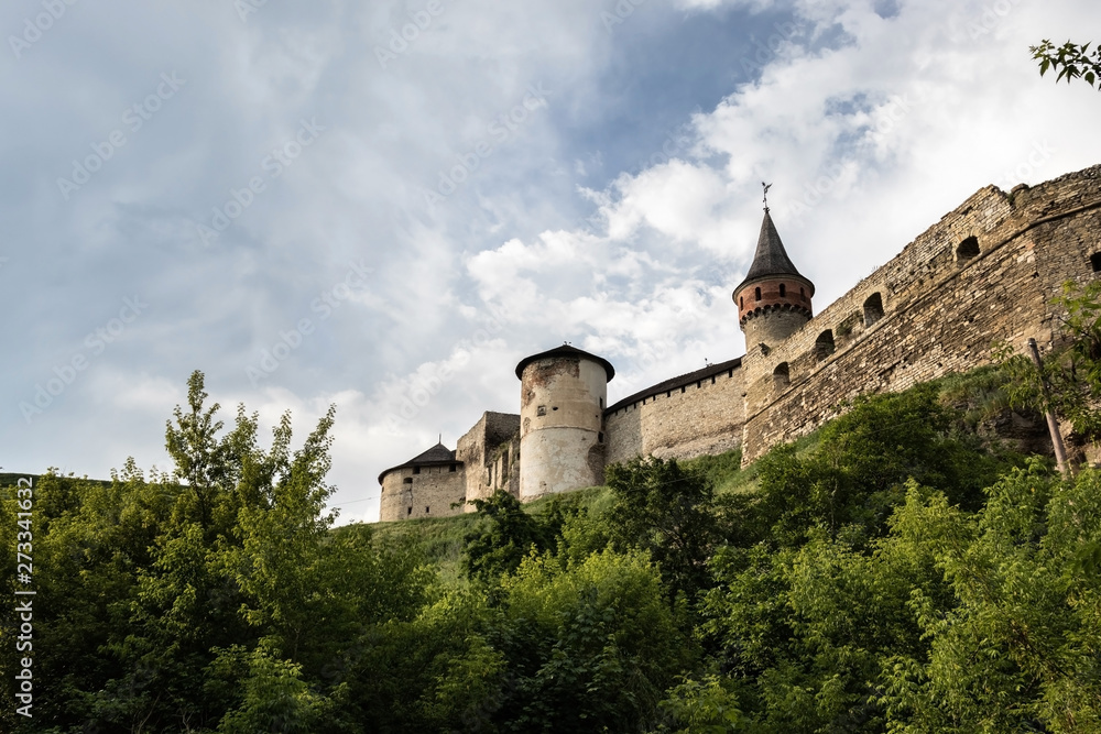 Towers and stone walls of the medieval Kamianets-Podilskyi fortress of the XVI century, rising on a hill against a background of cloudy sky. Ukraine.