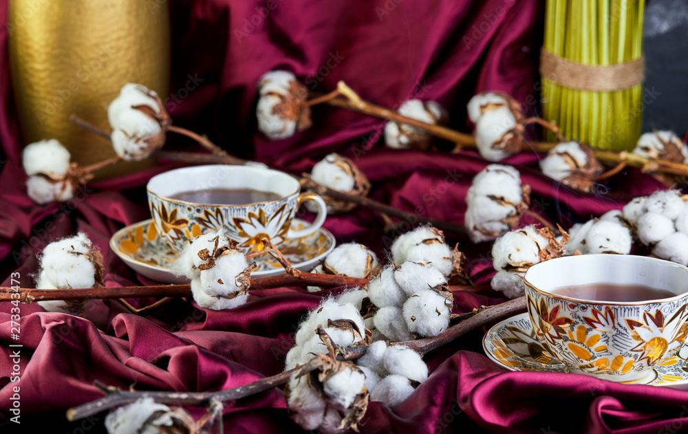 Cotton flowers lying on cloth and cups of tea. The concept of the Eastern lifestyle.