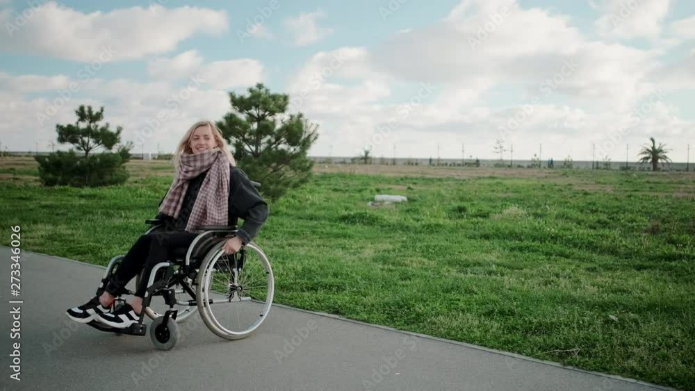 Happy young woman is whirling her body in wheelchair in park area in sunny day Happy young woman is whirling her body in wheelchair in park area in sunny day