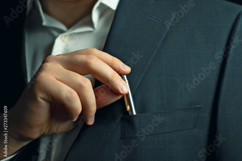  businessman in a suit taking or putting  a pen from the breast pocket of his jacket