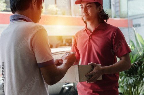 young woman customer appending signature in digital mobile phone receiving parcel post box from courier with home delivery service man smiling face in red uniform at home, express delivery concept
