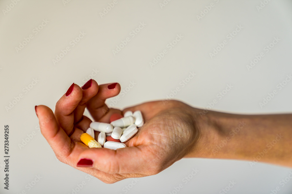 Female hand with red fingernails offering pills and capsules in different colors on open hand with white background