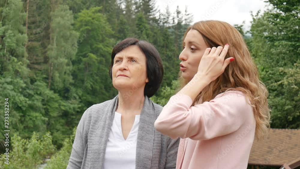An elderly retired mother and adult daughter are talking against the background of wooded mountains. Holidays in the mountains, mother's day, two generations An elderly retired mother and adult daughter are talking against the background of wooded mountains. Holidays in the mountains, mother's day, two generations