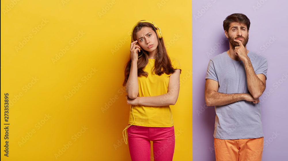European couple dont speak to each other after quarrel, woman ignores husband listening music in headphones, pensive serious guy holds chin, contemplates about something. Two colored background European couple dont speak to each other after quarrel, woman ignores husband listening music in headphones, pensive serious guy holds chin, contemplates about something. Two colored background