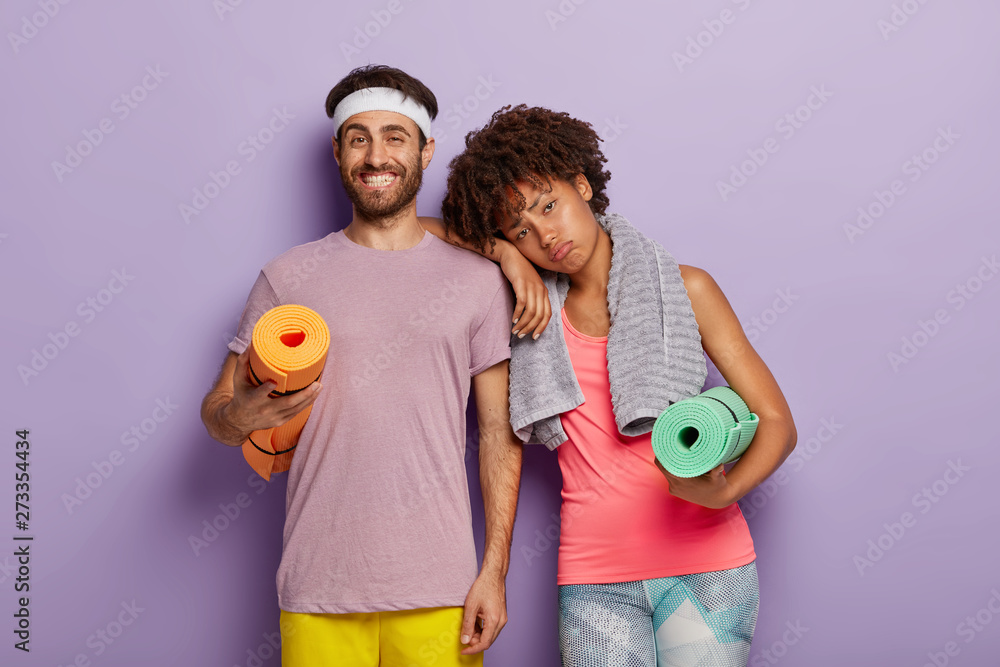 Unhappy displeased dark skinned female leans at shoulder on coach, being tired after exhausting training, carries rolled karemat under arm, isolated against purple background. Sport and motivation Unhappy displeased dark skinned female leans at shoulder on coach, being tired after exhausting training, carries rolled karemat under arm, isolated against purple background. Sport and motivation