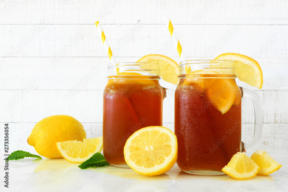 Fototapeta premium Iced tea in mason jar glasses with lemons. Side view on a white wood background.
