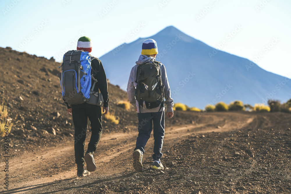 Two young boys walking on a path toward the volcano Teide A couple of tourist child climbing mountain together Italian and Canary island flag on wool caps. Adventure trip togetherness open air concept