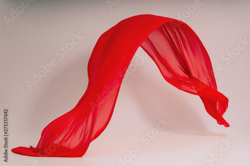 Red fabric on a white background. Levitation of red fabric in the photo studio. Soaring piece of cotton fabric. Flying colored fabric on a light background