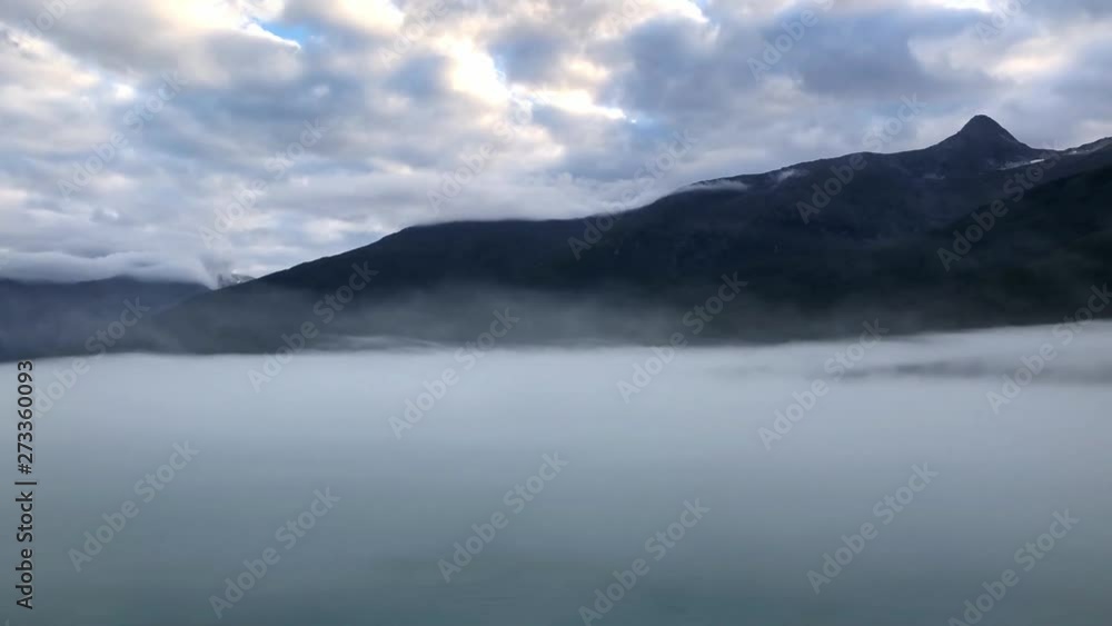 Pan right: Mist covered Alaskan ocean with majestic mountain landscape on horizon Pan right: Mist covered Alaskan ocean with majestic mountain landscape on horizon
