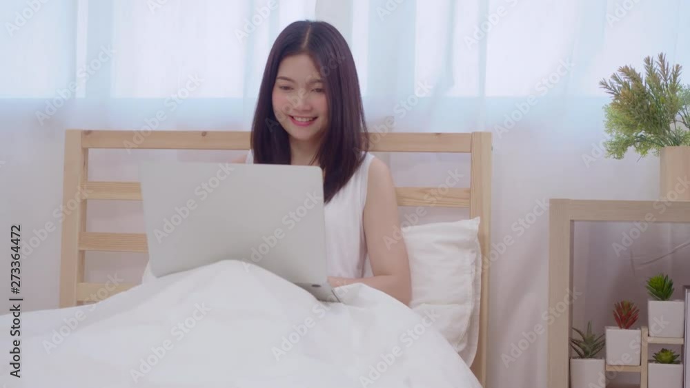 Young business freelance Asian woman working on laptop checking social media while lying on the bed when relax in bedroom at home. Lifestyle women at house concept. Young business freelance Asian woman working on laptop checking social media while lying on the bed when relax in bedroom at home. Lifestyle women at house concept.