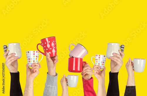 many raised hands up with ceramic cups on a yellow background