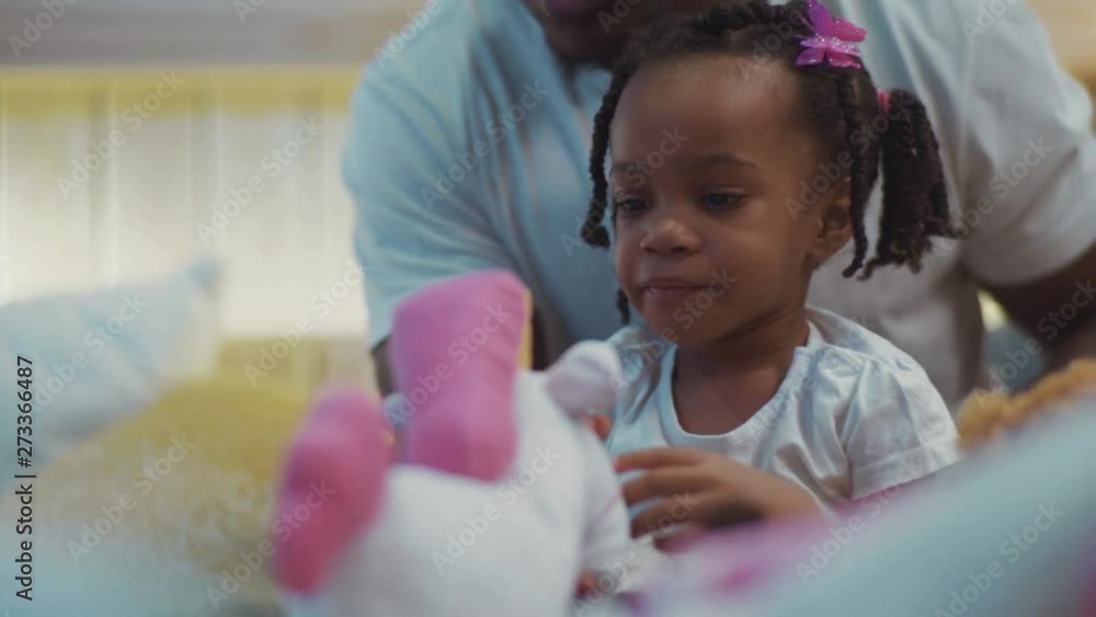 Close-up portrait of wonderful little afro-american black girl with braids sitting with father on bed looking around. Close-up portrait of wonderful little afro-american black girl with braids sitting with father on bed looking around.