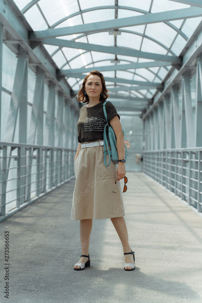 Beautiful stylish woman with backpack, smiling, happy, street style, beige skirt, green t-shirt.