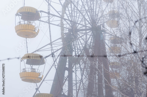 selective focus of ferris wheel attractionron behind barbed wire in fog in winter abandoned amusement park in Pripyt, Chernobyl zone of alienation