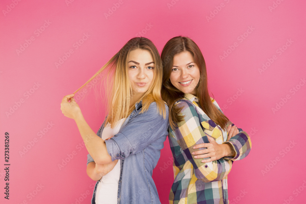 two beautiful girls friends smiling and looking at the camera, pink background two beautiful girls friends smiling and looking at the camera, pink background