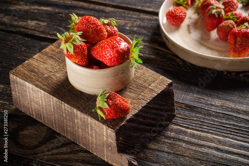 Ripe strawberries in a cup and on a ceramic plate lie on a wooden background.