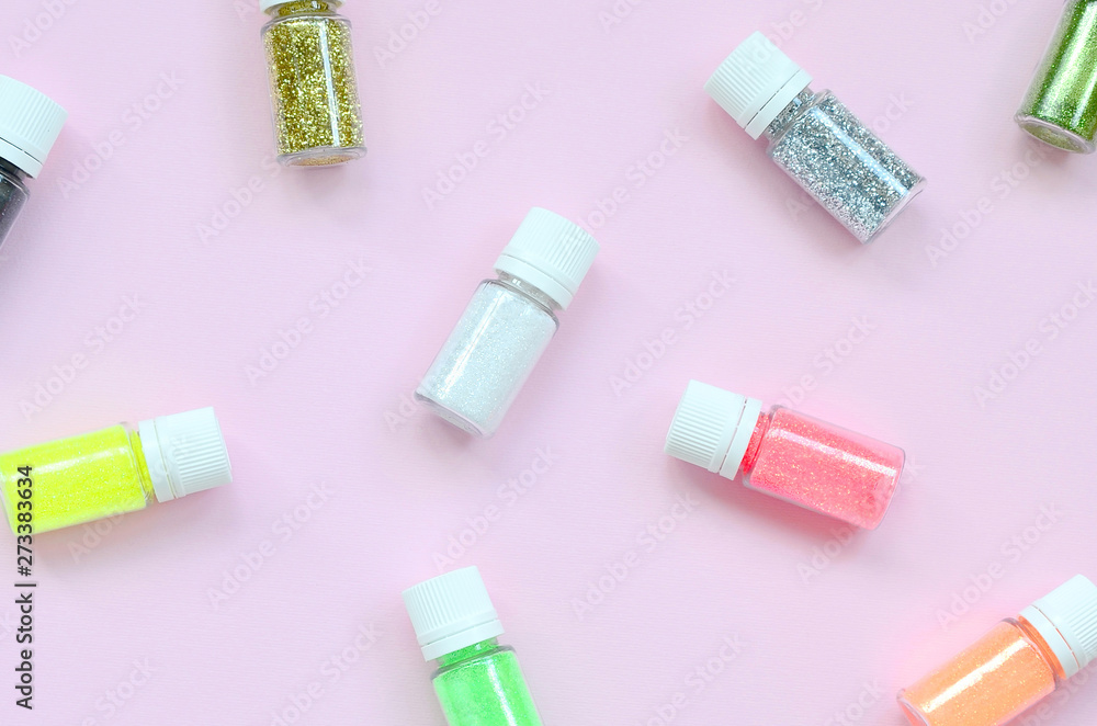 A flat lay pattern with colorful glitter bottles lies on pastel pink background A flat lay pattern with colorful glitter bottles lies on pastel pink background