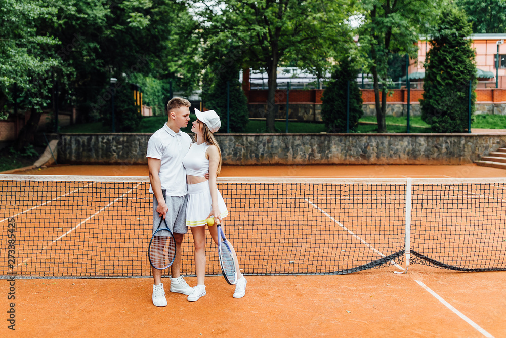 Tennis sport - couple relaxing after playing game of tennis outside in summer. Hugging couple.