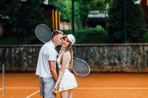 Enjoying spending time together. Photo of  back, beautiful young couple , man kiss his woman on the tennis court with smile. © Тарас Нагирняк