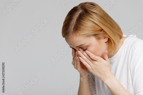 Young woman has a problem with contact lenses, rubbing her swollen eyes due to pollen, dust allergy. Dry eye syndrome, watery, itching. Isolated on grey background, free space. 