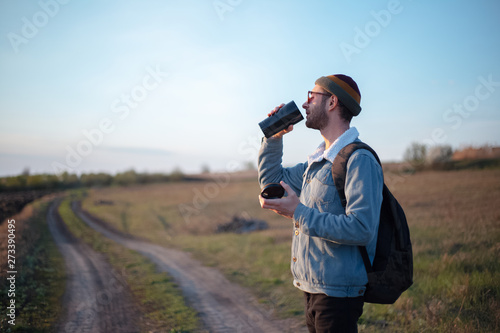 Young man in the green fields with thermo cup with coffee