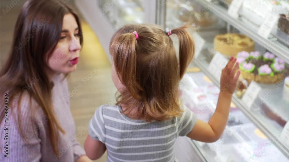 Cute girl and her mom choose delicious cakes for dessert in coffee shop Cute girl and her mom choose delicious cakes for dessert in coffee shop