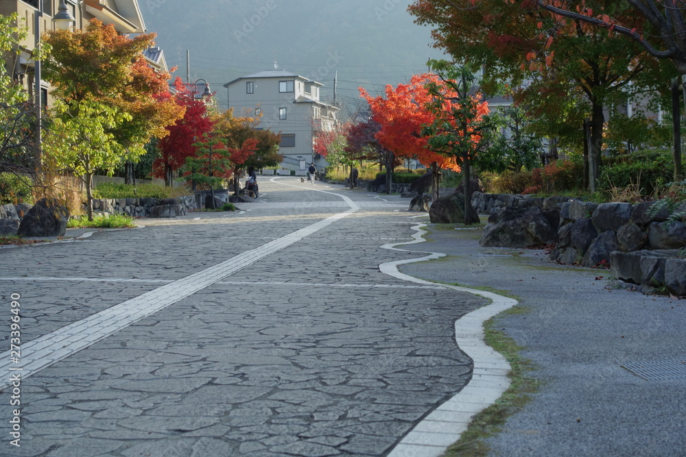 住宅地の石畳と散歩する人影が見える秋の風景です
