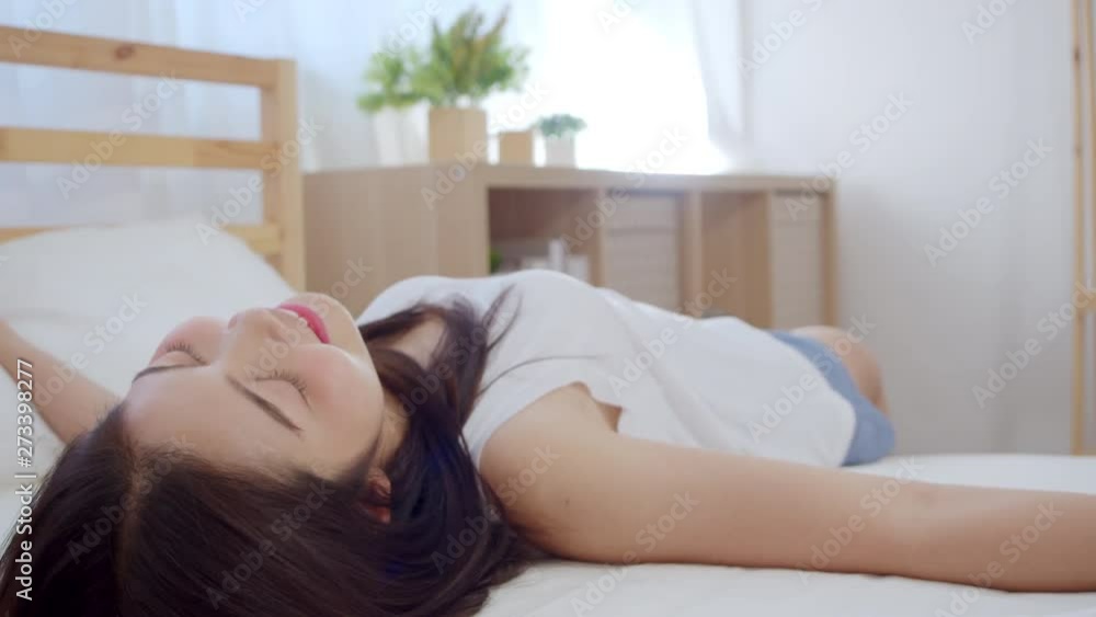 Asian woman smiling funny happy lying on bed in bedroom, Beautiful japanese female using relax time after wake up at home. Lifestyle women using relax time at home concept. Slow motion shot. Asian woman smiling funny happy lying on bed in bedroom, Beautiful japanese female using relax time after wake up at home. Lifestyle women using relax time at home concept. Slow motion shot.