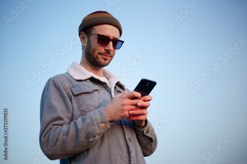 Portrait of modern guy with smartphone in hands on background of blue sky © Lalandrew