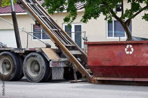 Empty roll-off construction dumpster being unloaded from truck at residential construction site