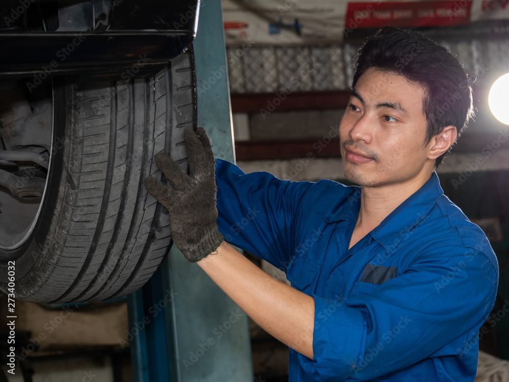 Handsome asian mechanic inspecting wheel and suspension detail of lifted automobile at repair garage. Handsome asian mechanic inspecting wheel and suspension detail of lifted automobile at repair garage.