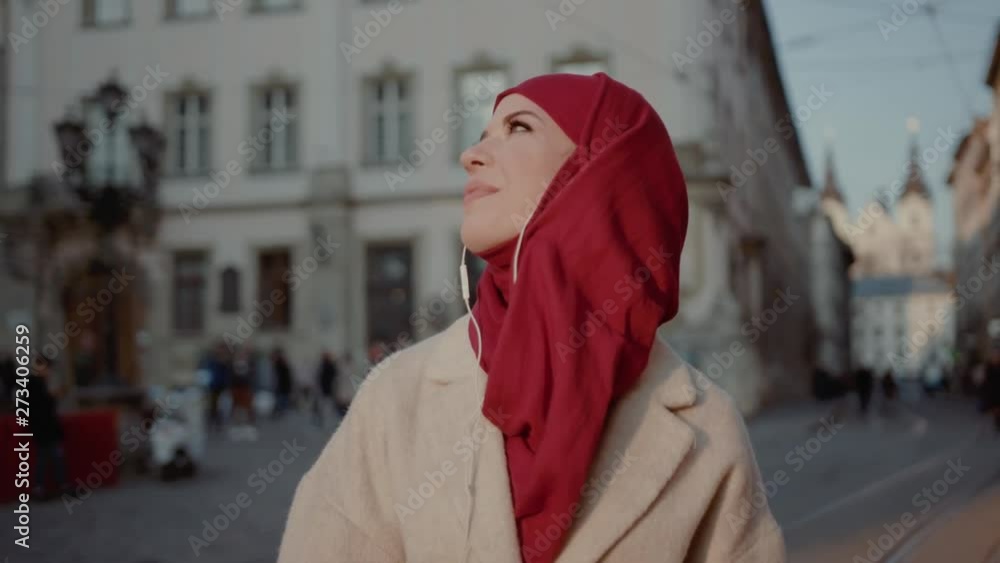 Exciting Muslim young lady enjoying music wearing hijab and earphones. Portrait of beauty arab girl using a smartphone admiring sunset in the city center. Exciting Muslim young lady enjoying music wearing hijab and earphones. Portrait of beauty arab girl using a smartphone admiring sunset in the city center.