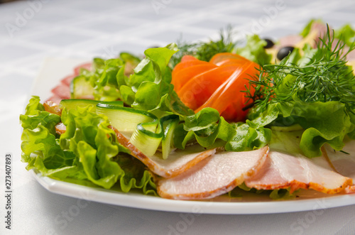 banquet cutting with ham, meat delicacies, cheese, sausage smoked, olive, lettuce and tomato on white dish