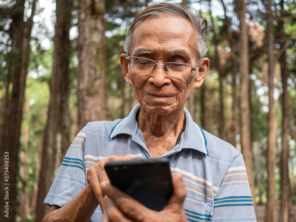 Elderly Asian man using smartphone in the garden. Elderly Asian man using smartphone in the garden.