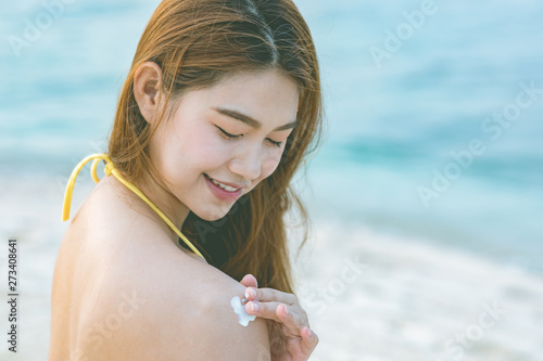 Beauty Attractive Asian young woman smile with healthy skin applying sunscreen lotion on her shoulder on the beach for UV protection,Skin care Concept