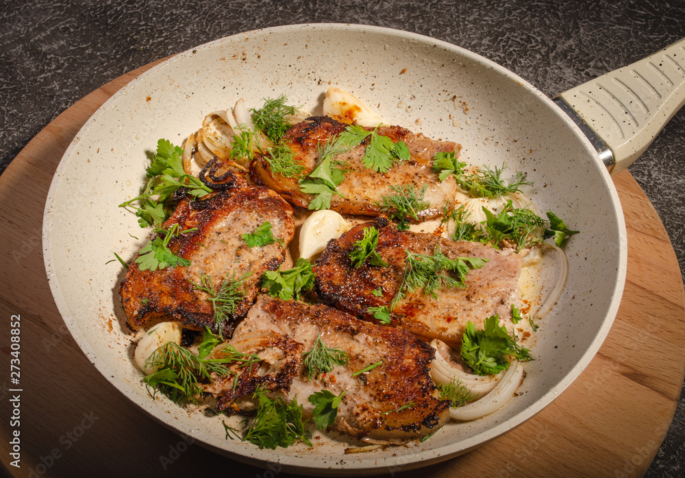 Bacon fried with onions and herbs in a pan of light color on a cutting Board and a dark background Bacon fried with onions and herbs in a pan of light color on a cutting Board and a dark background