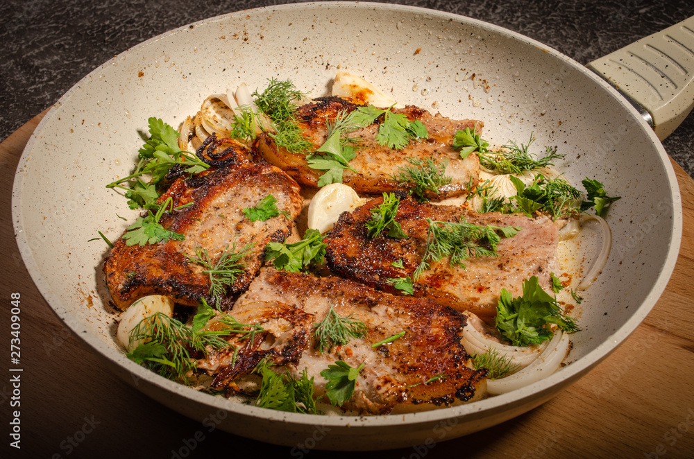Bacon fried with onions and herbs in a pan of light color on a cutting Board and a dark background Bacon fried with onions and herbs in a pan of light color on a cutting Board and a dark background