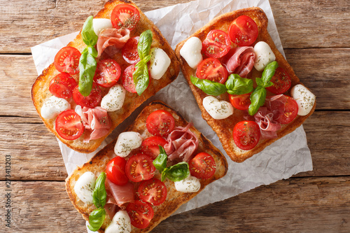 Italian open sandwiches with mozzarella, tomatoes, ham and basil closeup. Horizontal top view