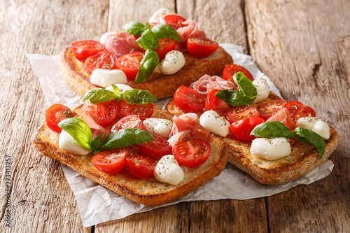 Schilderij op canvas Ciabatta summer toasts with mozzarella, tomatoes, ham and basil close-up on the table