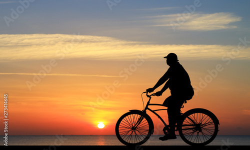 Silhouette man and bike relaxing on blurry sunrise sky background.