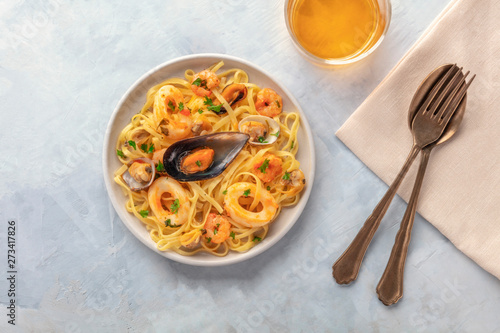Seafood pasta. An overhead photo of tagliolini with mussels, shrimps, clams and squid rings with a glass of white wine