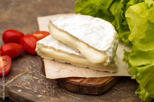 White mold cheese on a cutting board. Tomatoes and fresh lettuce. brie cheese. Tasty camembert