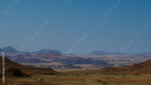 Namibian desert mountains with brown and yellow rock, ostrich in the foreground, dry desolate landscape