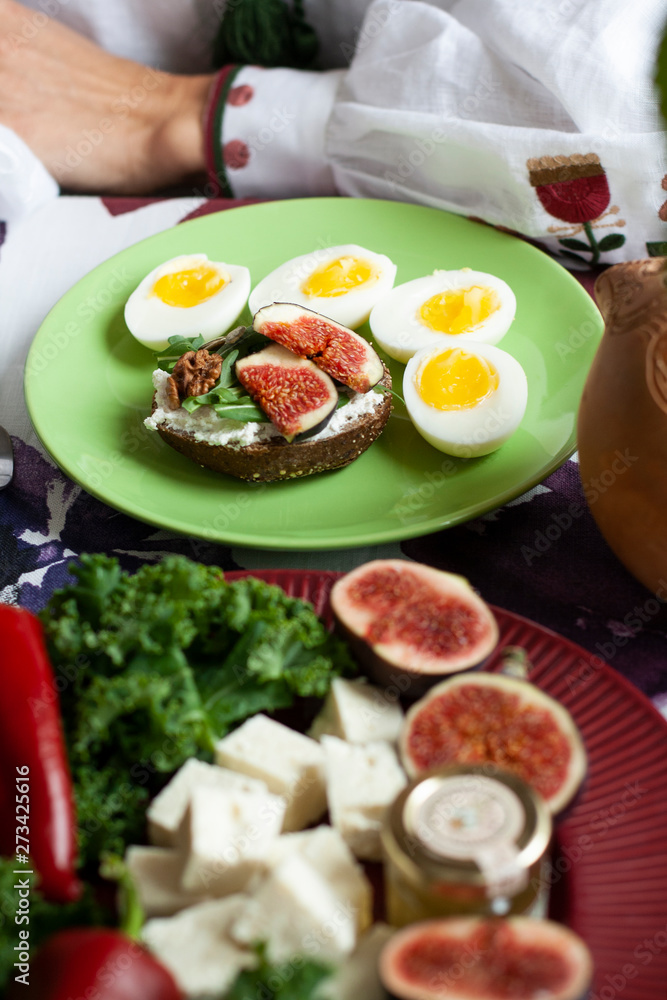 A gourmet lunch: a rye bread sandwich, cheese bites, sliced figs and boiled eggs.