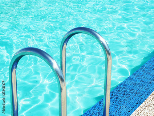 Pool side, blue pool water and metal ladder handrails.. © Olga