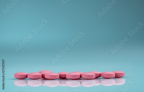 Round pink tablets pill on gradient background. Vitamins and minerals plus folic acid vitamin E and zinc in drug bottle on gradient background. Pink tablets pills for during and after pregnancy woman.