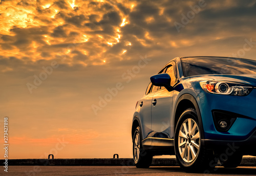 Blue compact SUV car with sport and modern design parked on concrete road by the sea with beautiful sunset sky.  Hybrid and electric car technology concept. Car parking space. Automotive industry. © Artinun