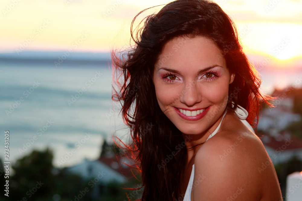 Jolie jeune femme brune devant un coucher de soleil et la mer
