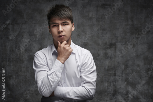 Serious Asian businessman ithinking of taking a loan on black background in white shirt. Kazakh student