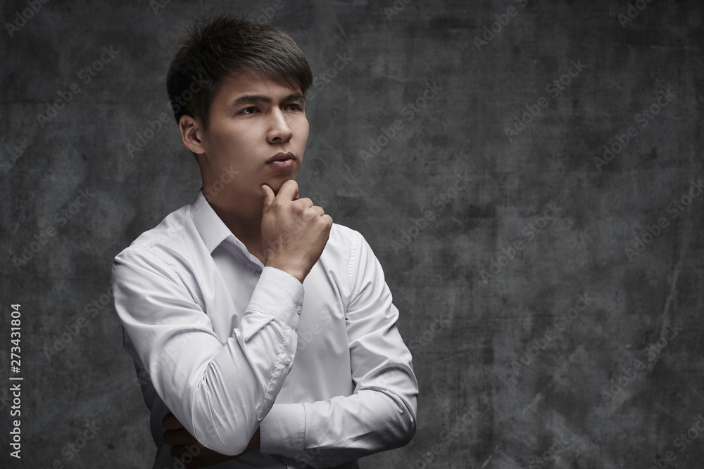 Serious Asian businessman ithinking of taking a loan on black background in white shirt. Kazakh student Serious Asian businessman ithinking of taking a loan on black background in white shirt. Kazakh student